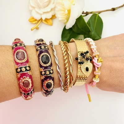 Pulseiras femininas variadas em diferentes materiais e cores no pulso de uma pessoa, com fundo de flores brancas e folhas verdes