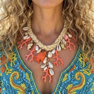 Colar artesanal com conchas, coral e pendente de peixe sobre camisola azul bordada