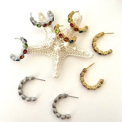 Brincos de argola dourados e prateados com pedras coloridas sobre estrela do mar branca