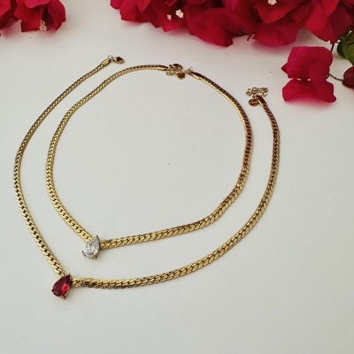 Conjunto de colar e pulseira dourados com pedras em forma de gota e flores vermelhas ao fundo