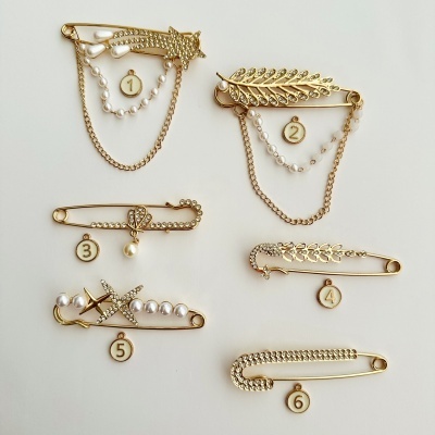 Alfinetes de segurança dourados decorados com pérolas, strass e números 1 a 6