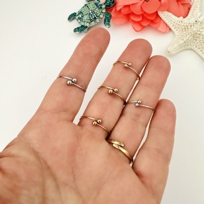 Conjunto de anéis finos dourados e prateados com duas esferas nas pontas em mão