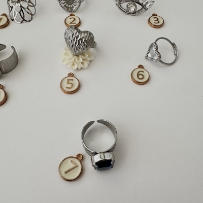 Conjunto de anéis em prata com diferentes desenhos e marcadores numerados sobre fundo branco.