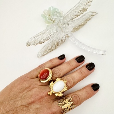 Mão com três anéis dourados e libélula decorativa transparente.