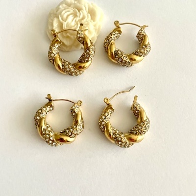 Dois pares de brincos dourados com brilhantes em fundo branco e flores decorativas