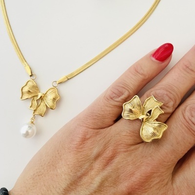 Colar dourado com flores e pérola e anel dourado em forma de flor numa mão com unhas vermelhas