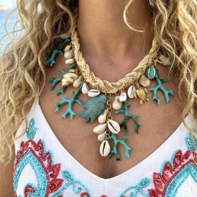 Colar com conchas, corais e figuras marinhas em mulher com vestido bordado branco.