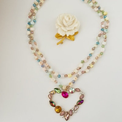 Colar de contas multicoloridas com pendente em forma de coração e broche de flor branca com folhas douradas