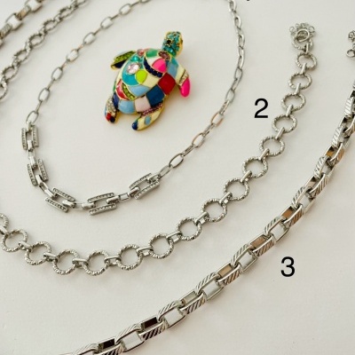 Três pulseiras prateadas e pulseira com pendente de tartaruga colorida sobre fundo branco.