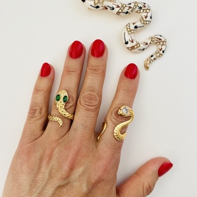 Anéis de serpente dourados com olhos verdes e pedra branca, unhas vermelhas, pulseira branca decorada com pedras