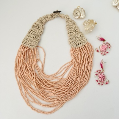 Colar de contas cor de pêssego com fecho de fio beige junto a brincos de caranguejo e conchas