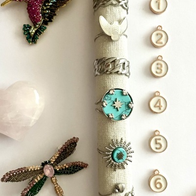 Anéis variados em suporte tecido branco com broches coloridos e etiquetas numeradas