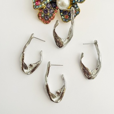 Brincos prateados com textura ondulada junto a broche floral colorido com pedras e pérola