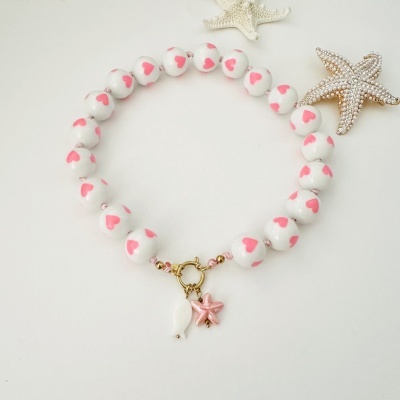 Pulseira com contas brancas com corações cor de rosa e pendentes de estrela do mar, peixe e concha
