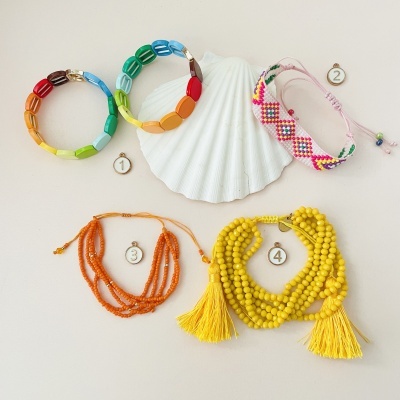 Cinco pulseiras coloridas sobre fundo claro, com concha ao centro