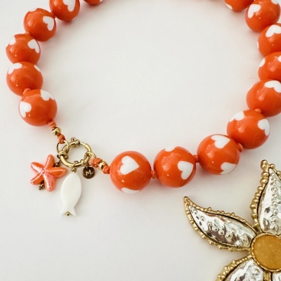 Pulseira laranja com corações brancos e pendentes temáticos em fundo branco