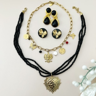 Conjunto de joias douradas e pretas com colares e brincos decorados com pendentes variados sobre fundo claro.