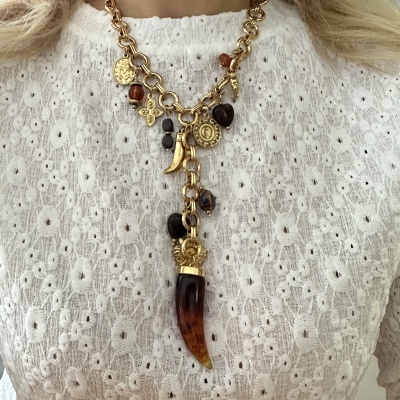 Colar dourado com pendentes sobre blusa branca rendada