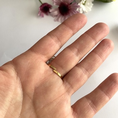 Anel dourado fino em mão com flores ao fundo