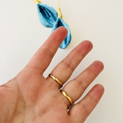 Brincos azuis e dourados e anéis dourados numa mão sobre fundo branco