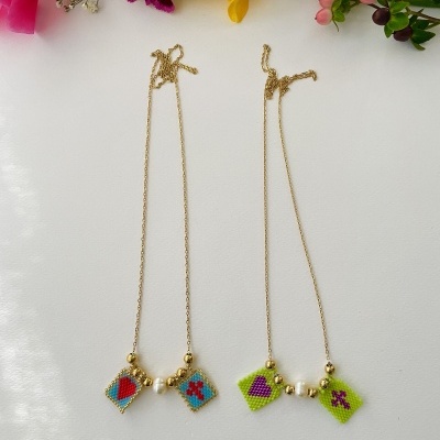 Dois colares com pendentes quadrados coloridos e contas douradas sobre fundo branco com flores