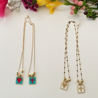 Quatro colares com pendentes quadrados decorados e correntes douradas, dispostos sobre fundo branco com flores coloridas no topo da imagem.