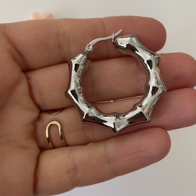 Brinco de argola prateado com design de bambu na mão.