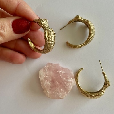 Brincos dourados em forma de crocodilo e pedra rosa sobre fundo branco