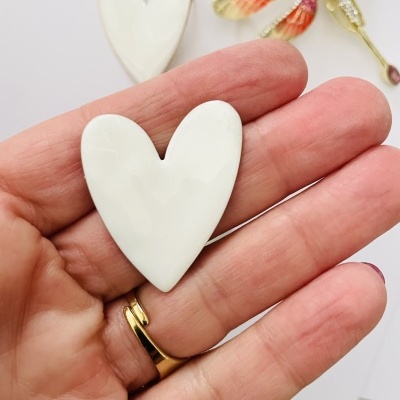 Corações brancos de porcelana na mão sobre fundo branco com objeto decorativo ao lado