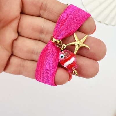 Pulseira elástica rosa com pendentes de estrela-do-mar dourada e peixe de vidro vermelho na mão