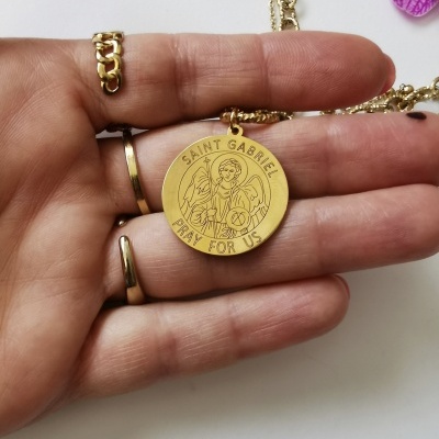 Colar dourado com medalhão redondo gravado de Saint Gabriel na mão