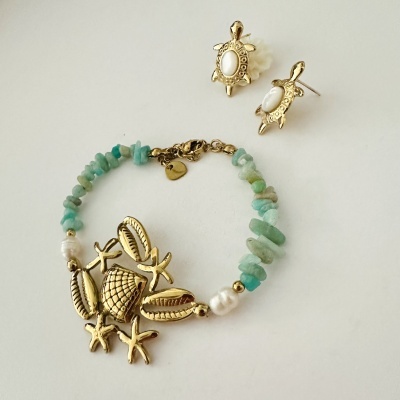 Brincos de tartaruga dourados com centro branco e pulseira com pedras azuis, contas brancas e pendente de caranguejo dourado.