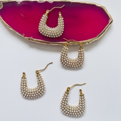 Brincos dourados com pérolas em padrão arqueado, quatro unidades, um em bandeja de ágata rosa e três sobre fundo branco.