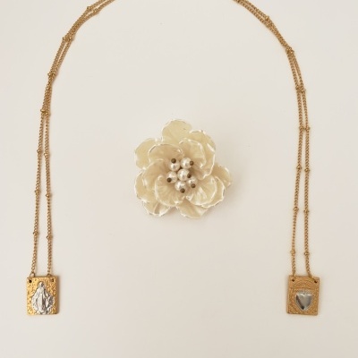 Colar dourado com dois pingentes em fundo branco e flor decorativa branca