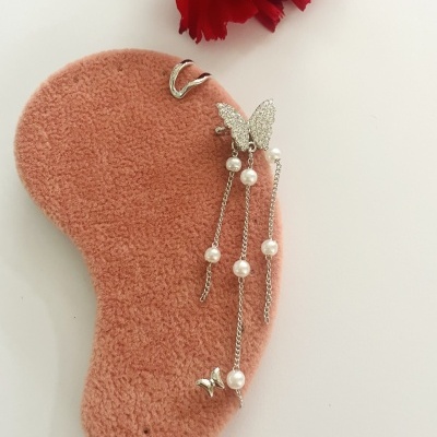 Brinco pendente prateado com borboletas e pérolas sobre suporte de veludo rosa.