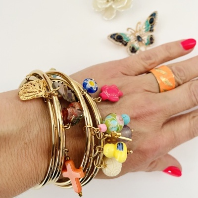 Pulseiras douradas com pendentes coloridos numa mão com anel laranja