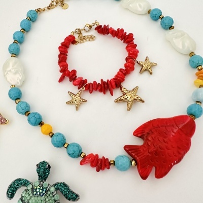 Pulseira colorida com peixe vermelho e estrelas douradas sobre fundo branco