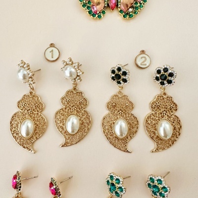 Seis pares de brincos em fundo bege, com pedras coloridas e detalhes dourados