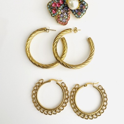 Dois pares de brincos de argola dourados e um broche de flor colorido com pérola central sobre fundo branco.