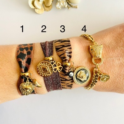Quatro pulseiras variadas em pulso com pendentes dourados e padrões animal print e tigre.