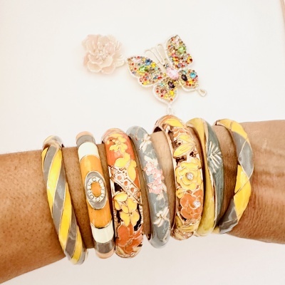 Pulseiras florais e coloridas num pulso com broche de borboleta e flor ao fundo