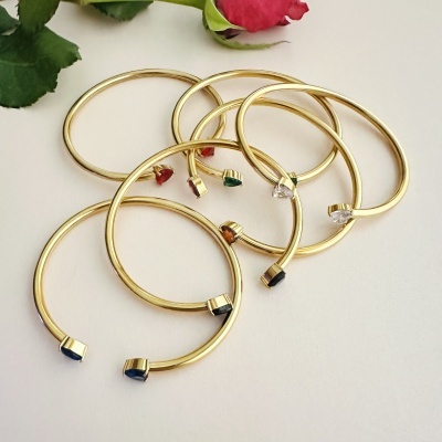 Pulseiras douradas com pedras coloridas e rosa vermelha
