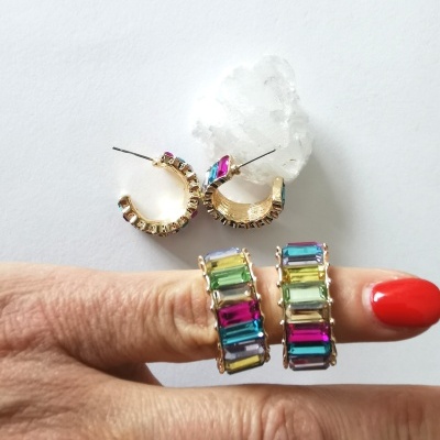 Brincos e anéis dourados com pedras coloridas retangulares em fundo branco.
