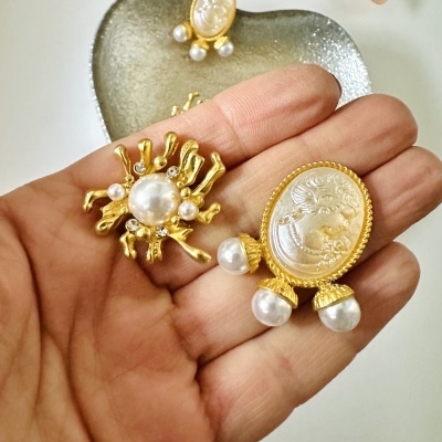 Brincos dourados com pérolas falsas e relevo oval branco