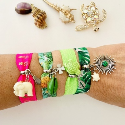 Pulso com pulseiras de tecido colorido e pendentes diversos em fundo branco com conchas e broche