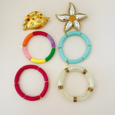 Seis brincos variados com argolas coloridas e pequenos em forma de concha e flor sobre fundo bege