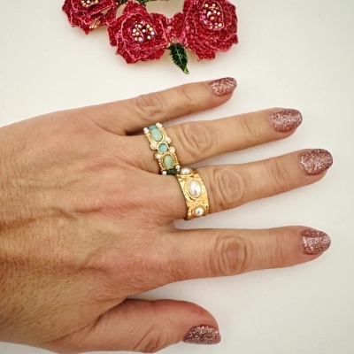 Mão com dois anéis dourados e unhas com verniz glitter rosa