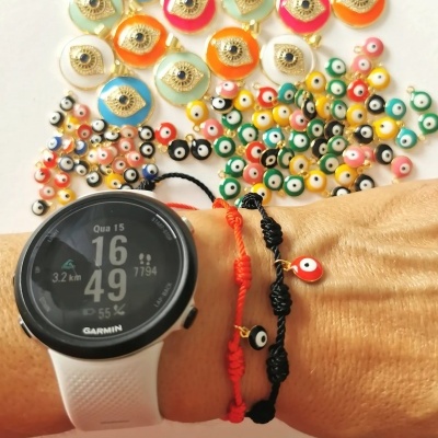 Pulso com relógio Garmin e pulseiras com amuletos olho grego e vários amuletos coloridos sobre fundo branco