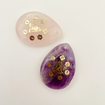 Dois pendentes em forma de lágrima com símbolos dourados, um rosa e um lilás