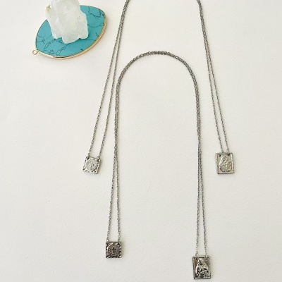 Colares de metal prateado com pendentes retangulares gravados e cristal branco sobre suporte azul